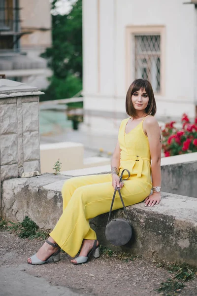 Beautiful woman in yellow jumpsuit posing on city streets.