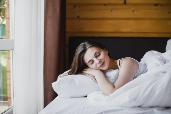 Young woman having good morning in bed in cozy wooden house.