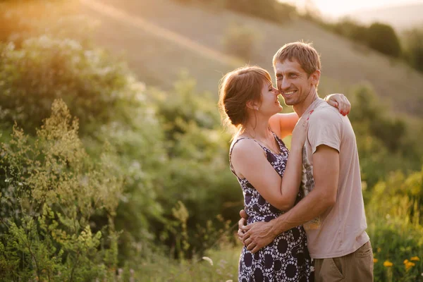 Happy young woman and man in romantic relationship hugging and kissing at sunset in a countryside.