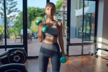 Spor salonunda dambıllarla egzersiz yapan genç atletik kız.