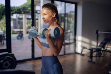 Spor salonunda dambıllarla egzersiz yapan genç atletik kız.