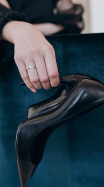 Parmağında yüzük olan bir kızın güzel eli siyah ayakkabılar tutuyor.