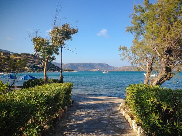 Elounda, Girit, Yunanistan - 12 Eylül 2017: Denize giden güzel bir yol. Tekneler dağların arka planında yüzer. Görünüm.
