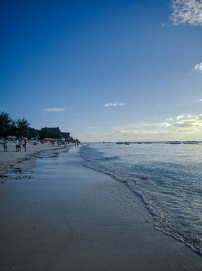 Zanzibar, Tanzanya - 3 Aralık 2019: Zanzibar 'daki Nungwi plajı, insanlar gün batımında sahilde eğleniyor. Güzel tropikal beyaz kumsal. Dikey.