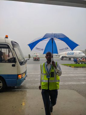 Zanzibar, Tanzanya - 5 Aralık 2019: Büyük mavi ve beyaz şemsiyeli Afrikalı bir adam yağmurlu havada otobüse binmeye yardım eder. Dikey.
