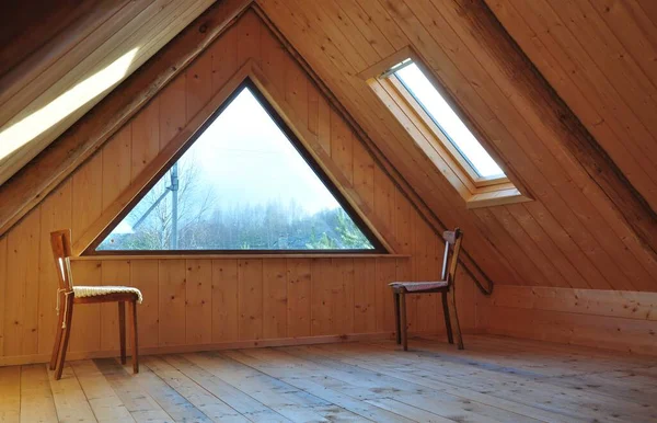 wooden interior with a triangular window and a skylight. two old chairs.