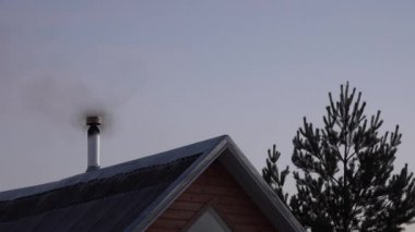 Duman, günbatımında ahşap bir evin metal borusundan gelir. Noel ağacıyla