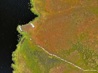 Patika yolu ve gölü olan havadan kırmızı bakır renkli bataklık. Kıyıdaki tekneler.