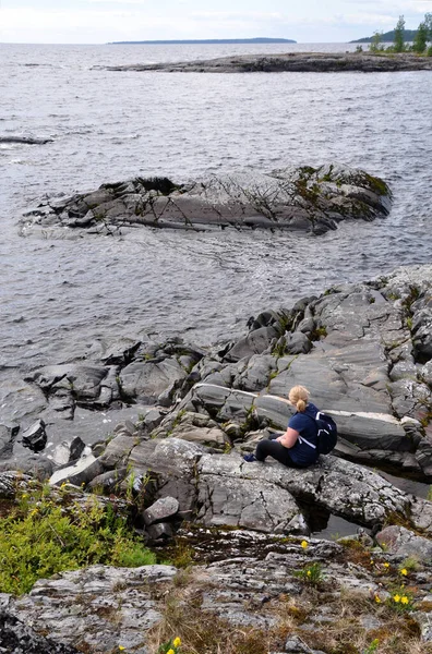 Mladá žena sedící na skalnatém pobřeží. Ladoga jezero Skerry Ruská Karelia — Stock fotografie