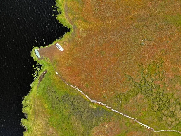 Patika yolu ve gölü olan havadan kırmızı bakır renkli bataklık. Kıyıdaki tekneler.