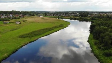 Sahilde yeşil tarlaları ve küçük ahşap kasabası olan geniş bir nehir. Hava görünümü.