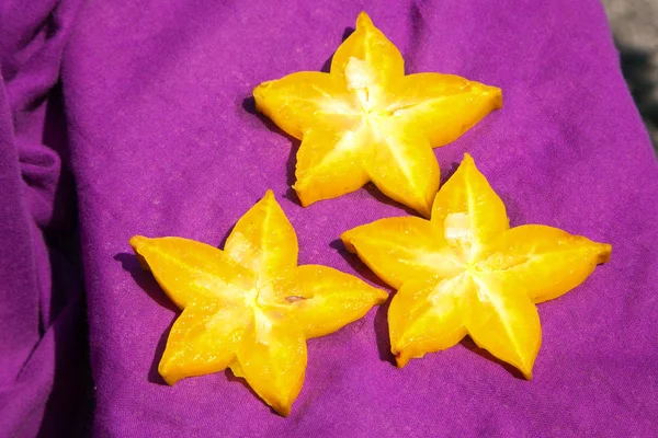Three slices of star fruit on a violet background