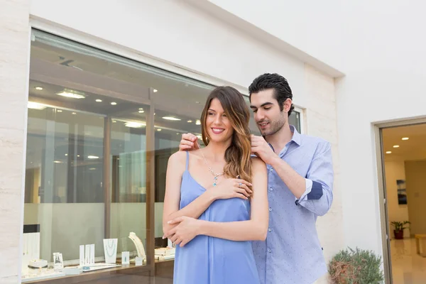 Handsome man putting necklace on his girlfriend neck in front of a jewelry store