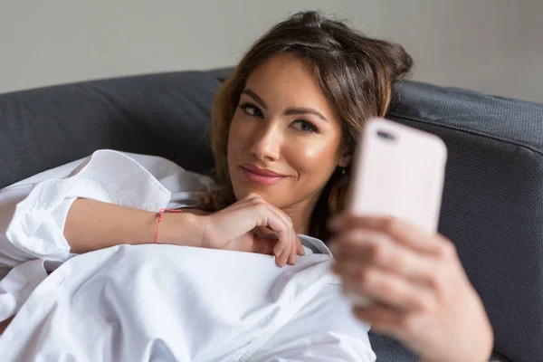 Ελκυστική νεαρή γυναίκα παίρνει selfie στο κρεβάτι — Φωτογραφία Αρχείου