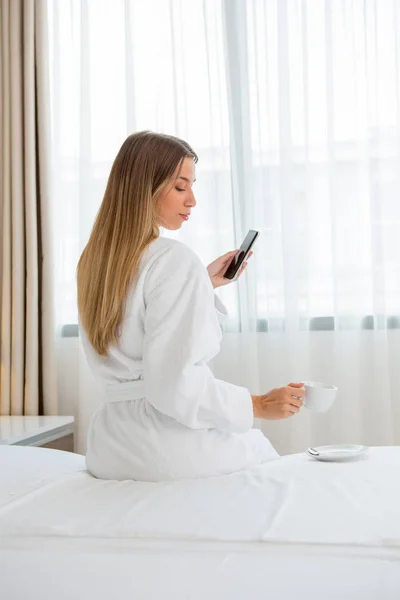 Schöne Frau sitzt auf dem Bett und genießt den morgendlichen Kaffee — Stockfoto