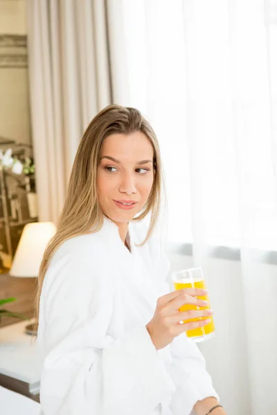 Mooie vrouw zittend op het bed drinken sinaasappelsap — Stockfoto