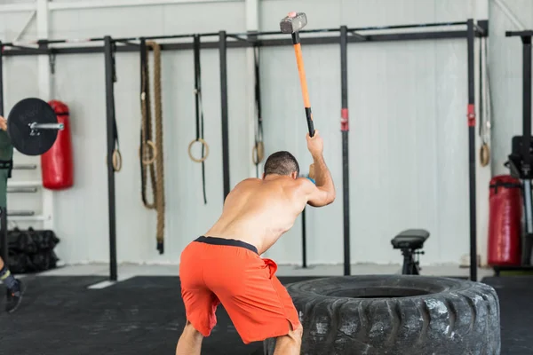 Sport fitness man hitting tractor tire with a sledgehammer