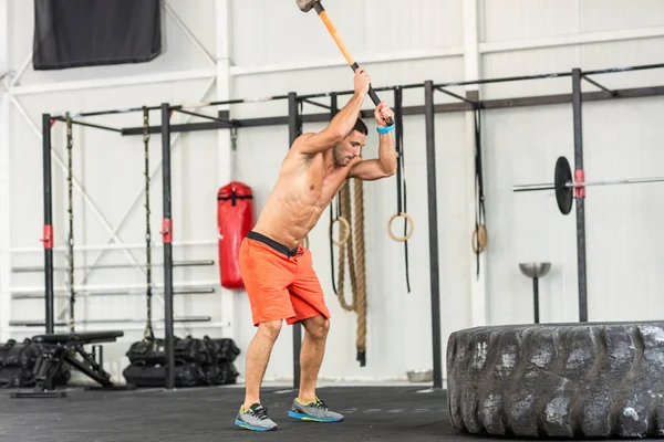 Sport fitness man hitting tractor tire with a sledgehammer