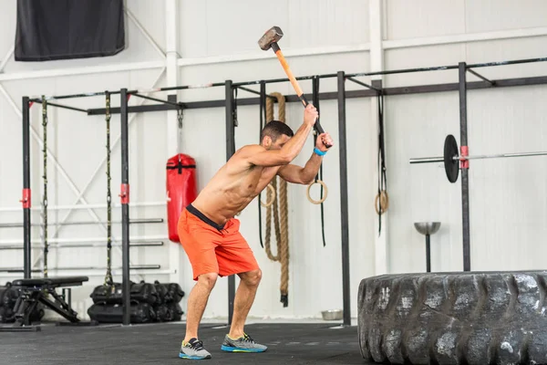 Sport fitness man hitting tractor tire with a sledgehammer