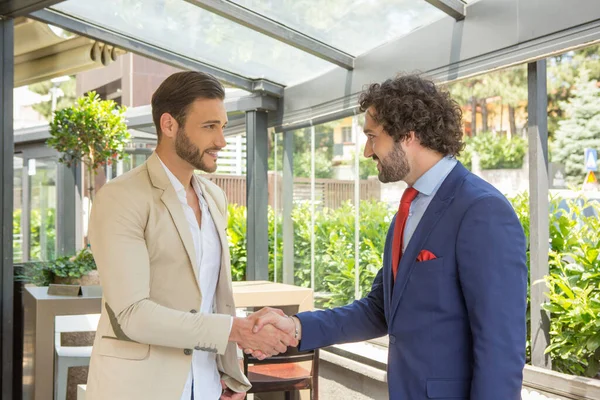 Two businessmen shaking hands in garden restaurant