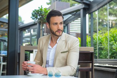 Takım elbiseli yakışıklı genç işadamı kahve içiyor.