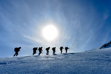 climbers march towards the summit on a windy winter day clipart