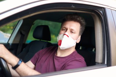 Coronavirus salgını sırasında tıbbi solunum cihazında araba kullanan bir adam maskeli bir taksi şoförü, virüsten korunan bir adam. Beyaz arabalı bir sürücü, elini direksiyona koyup açık pencereden dışarı bakıyor. Karantina, covid-19.