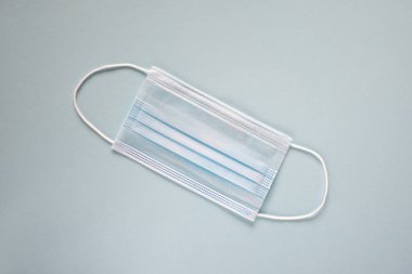 Coronavirus önleme maskesi. Sosyal mesafe, Covid-19 karantinası sırasında kendini izole etme. Güvenli nefes alma maskesi düzeni, üst görünüm, düz yatış, mavi arkaplan.