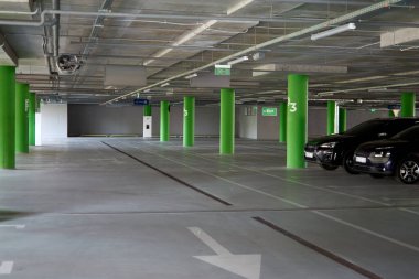 Yeraltı boş otoparkı. Tepesinde ışıklar ve tavandan sarkan bir çıkış işareti var. Arabalar için ücretsiz park