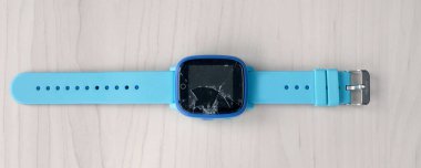 Çok renkli çocuklar ahşap bir masada kırık ekranlı akıllı saat telefonu. Çocuklar için teknoloji. Giyilebilir alet konsepti. Üst manzara, yakın plan. Okul saati..