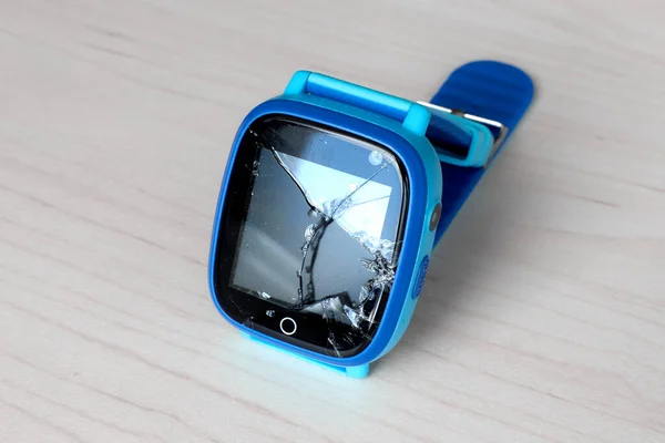 Multicolored kids smart watch phone with broken screen on a light wooden table. Technology for children. Wearable gadget concept. Top view, close-up. Time clock for school.