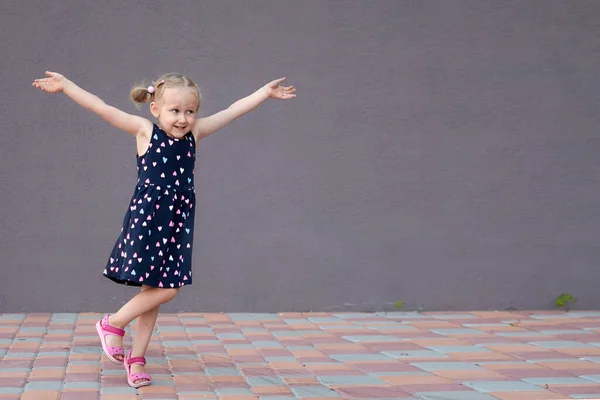 Portrait of a happy liitle blond girl close-up. 3 yaers caucasian todler girl smiling at outdoors walk. Stone wall background with copy space. Kid dancing and shouting showing different emotions — Stock Photo, Image