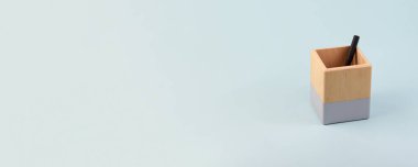 Soluk tek renkli mavi arka planda kalem tutucu. İş için ofis malzemeleriyle geniş pankart kopyalama alanı.