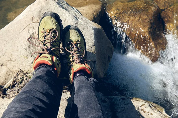 Hiking boots in outdoor action. Top View of Boot on the trail. Close-up Legs In Jeans And sport trekking shoes on rocky srones of Mountain river waterfall.