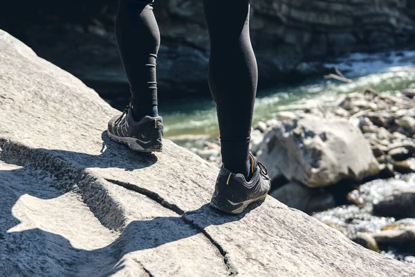 Man climbs mountain steam river. Sporty clothes and backpack. Hiking boots in outdoor action. Top View of Boot on the trail. Close-up Legs In sport trekking shoes on rocky stones of Mountain river waterfall.