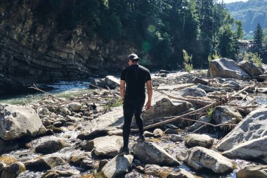 Adam dağ buhar nehrine tırmanıyor. Spor kıyafetler ve sırt çantası. Yürüyüş botları dışarıda. Top View of Boot yolda. Spor yürüyüş ayakkabılarıyla Dağ nehri şelalesinin kayalık taşlarında.