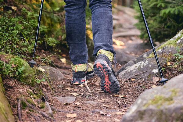 Женщина лазает в сапогах для пеших прогулок на природе. Вид сверху на трассу. Крупный план Ноги в джинсах и спортивные треккинговые туфли на скалистых камнях горного леса.