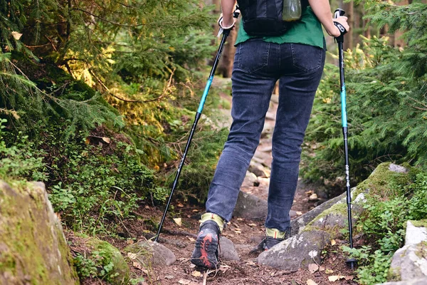 Kobieta wspina się w butach turystycznych w akcji na świeżym powietrzu. Góra Widok Boot na szlaku. Close-up Nogi w dżinsach i sportowe buty trekkingowe na kamieniach skalistych lasów górskich — Zdjęcie stockowe