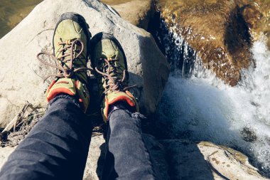 Yürüyüş botları dışarıda. Top View of Boot yolda. Kotlu bacaklar ve dağ nehri şelalesinin kayalık kayalıklarında spor yürüyüş ayakkabıları..