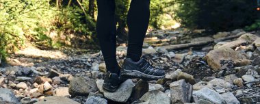 Adam dağ buhar nehrine tırmanıyor. Spor kıyafetler ve sırt çantası. Yürüyüş botları dışarıda. Top View of Boot yolda. Spor yürüyüş ayakkabılarıyla Dağ nehri şelalesinin kayalık taşlarında.