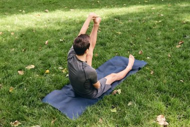Spor giyimli genç bir adam parkta yoga yapıyor. Asana 'yı dışarıda pratik yap. İnsanlar yeşil çimlerde yoga minderiyle egzersiz yapıyorlar. Fitness ve sağlıklı yaşam tarzı. Sakinlik ve meditasyon kavramı.