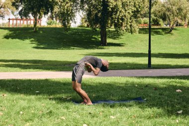 Spor giyimli genç bir adam parkta yoga yapıyor. Asana 'yı dışarıda pratik yap. Yeşil çimlerde yoga minderiyle egzersiz yapan insanlar. Dsun selamları içinde güçlü bir beyaz adam..