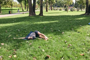 Spor giyimli genç bir adam parkta yoga yapıyor. Asana 'yı dışarıda pratik yap. İnsanlar yeşil çimlerde yoga minderiyle egzersiz yapıyorlar. Fitness ve sağlıklı yaşam tarzı. Sakinlik ve meditasyon kavramı.