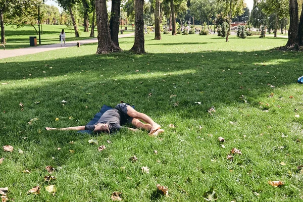 Spor giyimli genç bir adam parkta yoga yapıyor. Asana 'yı dışarıda pratik yap. İnsanlar yeşil çimlerde yoga minderiyle egzersiz yapıyorlar. Fitness ve sağlıklı yaşam tarzı. Sakinlik ve meditasyon kavramı.