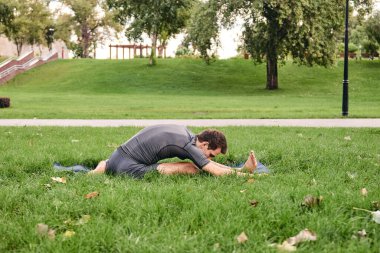 Spor giyimli genç bir adam parkta yoga yapıyor. Janu Sirshasana asana 'nın dizinden dizine kadar dışarıda poz ver. İnsanlar yeşil çimlerde yoga minderiyle egzersiz yapıyorlar. Fitness ve sağlıklı yaşam tarzı.