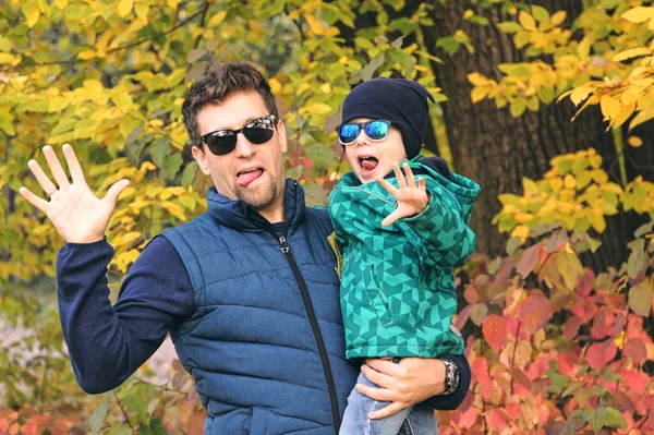 Autumn family walk in forest. Beautiful park with dry yellow leaves. Son and father holding hands.