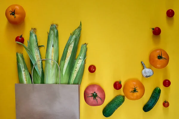 Χαρτοσακούλα με διάφορα είδη παντοπωλείου σε κίτρινο φόντο. Top view ντοματίνια, αγγούρια, σκόρδο. Κτήμα συγκομιδής καλαμποκιού, φρέσκα vegan παράδοση πράσινων τροφίμων — Φωτογραφία Αρχείου
