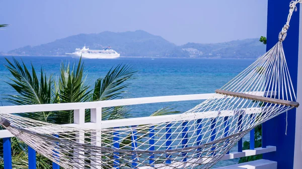 The white hammock hanging on terrace front of the beach, view of the mountain, a yacht in blue sea