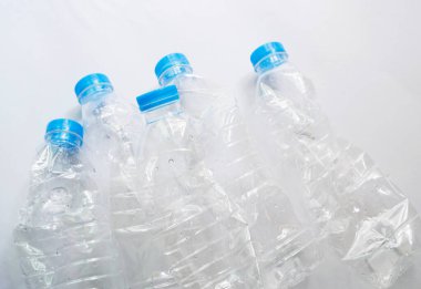 Beyaz zemin üzerinde mavi kapaklı deforme olmuş temiz plastik su şişeleri sırası