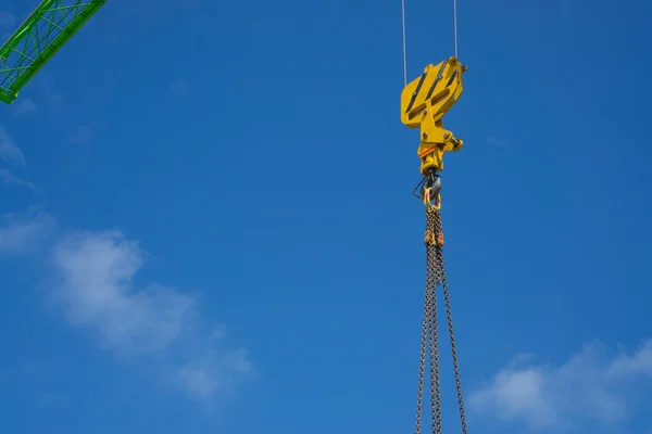 The upward view of yellow steel loop and chain hanging on the sling of a large green beam tower crane arm\'s under clear blue sky